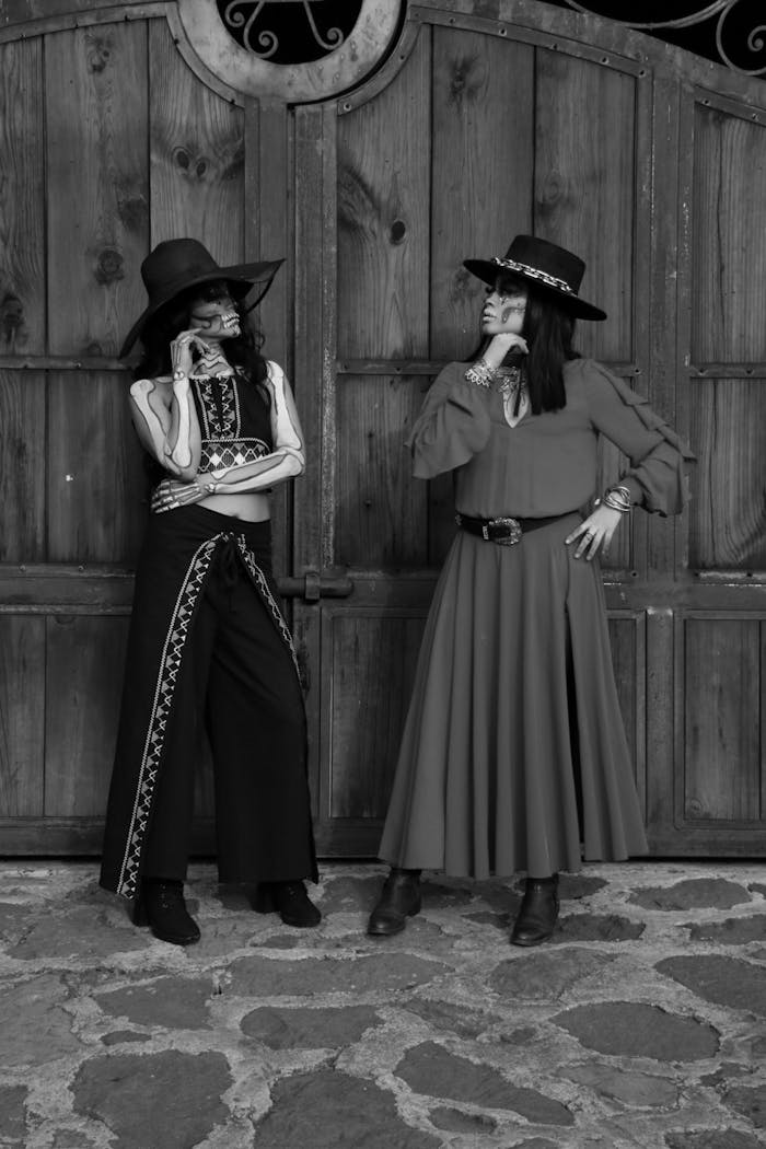 creative Two women in vintage western outfits pose against a rustic wooden gate.